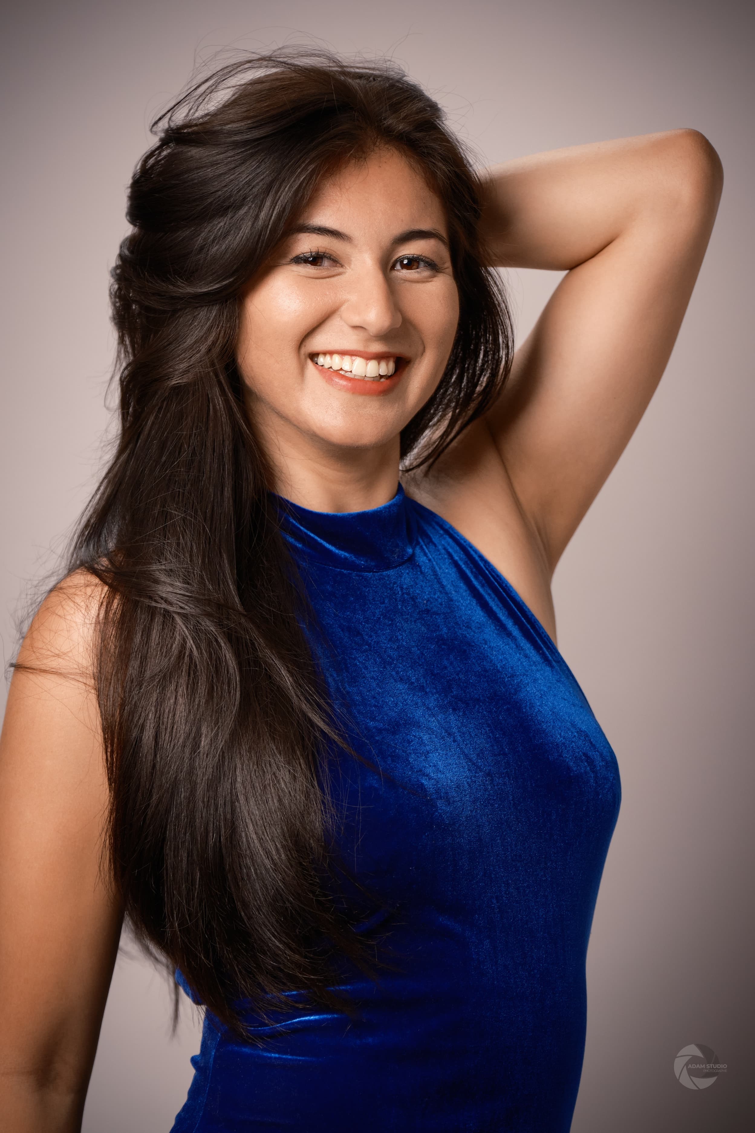Mae smiling, wearing a blue velvet dress, in an artistic portrait.